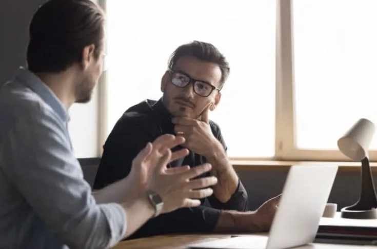 Two colleagues discuss work with a laptop beside them.